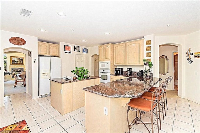 kitchen with white appliances, light brown cabinetry, a center island, and kitchen peninsula