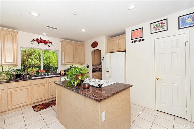 kitchen featuring a center island, light brown cabinets, white appliances, dark stone countertops, and light tile patterned flooring