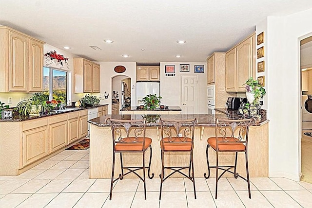 kitchen with a breakfast bar, white appliances, kitchen peninsula, and light brown cabinetry