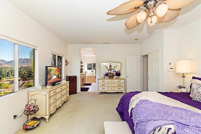 bedroom featuring light carpet, a mountain view, ensuite bathroom, and ceiling fan