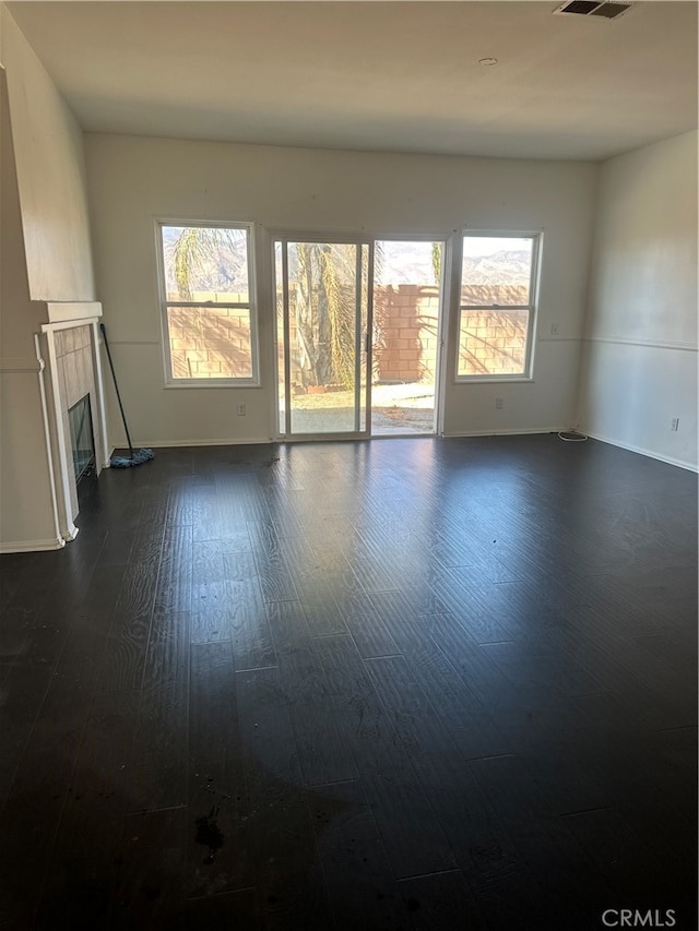 empty room with a tiled fireplace, dark hardwood / wood-style floors, and plenty of natural light