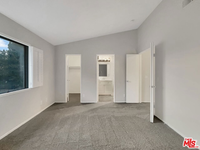 unfurnished bedroom featuring carpet floors, lofted ceiling, ensuite bath, and a walk in closet