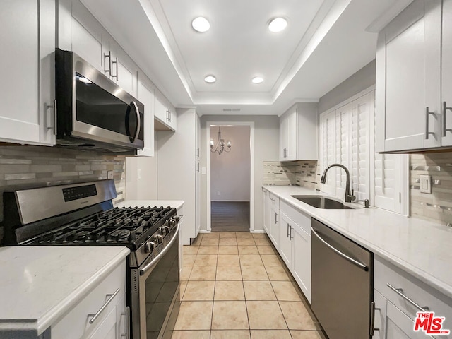 kitchen with white cabinetry, light tile patterned floors, stainless steel appliances, a tray ceiling, and sink