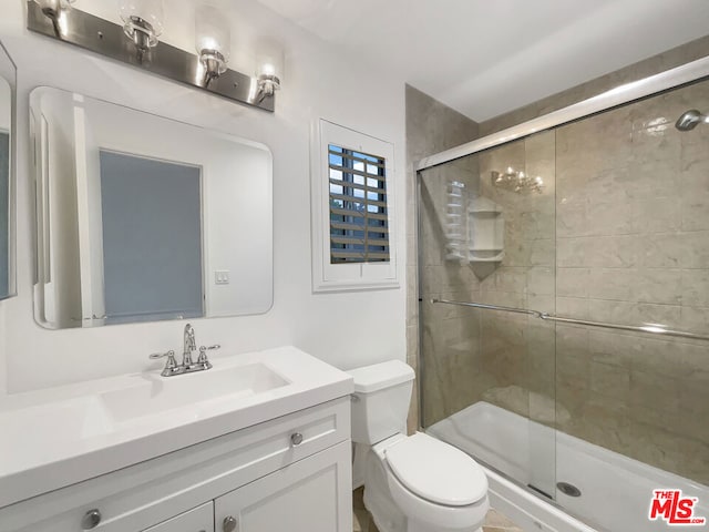 bathroom featuring a shower with shower door, vanity, and toilet