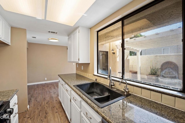 kitchen with hardwood / wood-style floors, range, sink, dark stone countertops, and white cabinetry