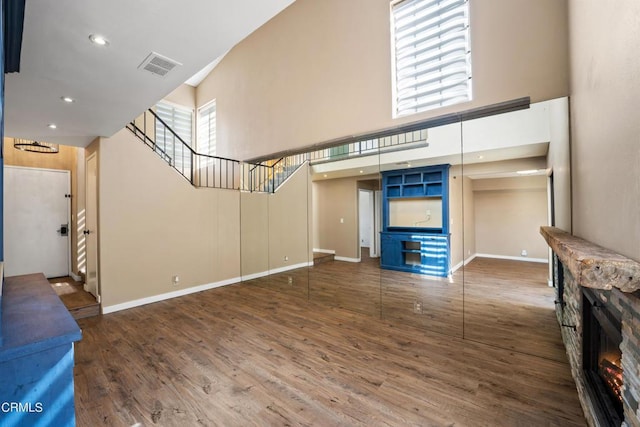 unfurnished living room with a stone fireplace, dark hardwood / wood-style floors, and a high ceiling