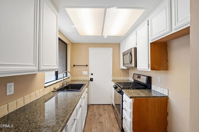 kitchen featuring appliances with stainless steel finishes, white cabinetry, dark stone counters, and sink