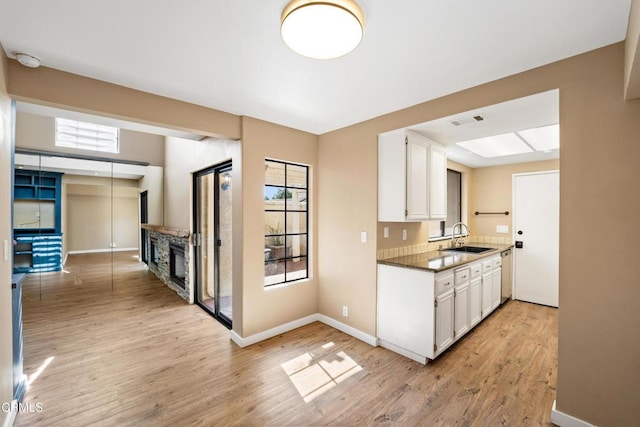 kitchen featuring sink, a stone fireplace, dark stone countertops, white cabinets, and light wood-type flooring