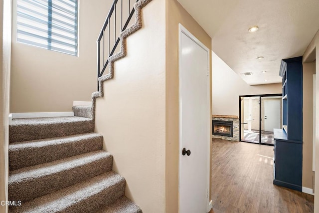 staircase featuring hardwood / wood-style flooring and a stone fireplace