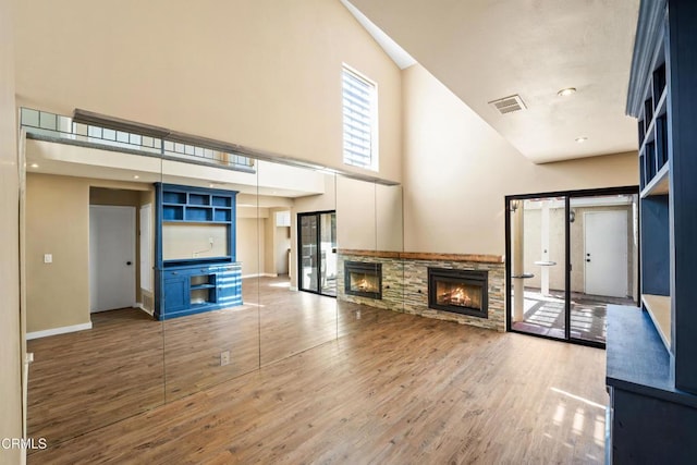 unfurnished living room with wood-type flooring, a towering ceiling, and a stone fireplace