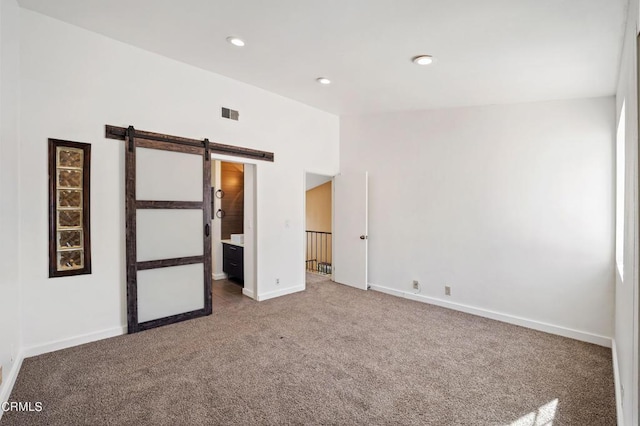 unfurnished bedroom featuring carpet, a barn door, and ensuite bathroom