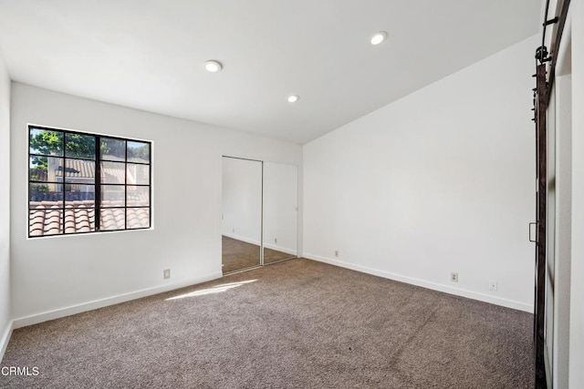 spare room featuring a barn door and dark carpet