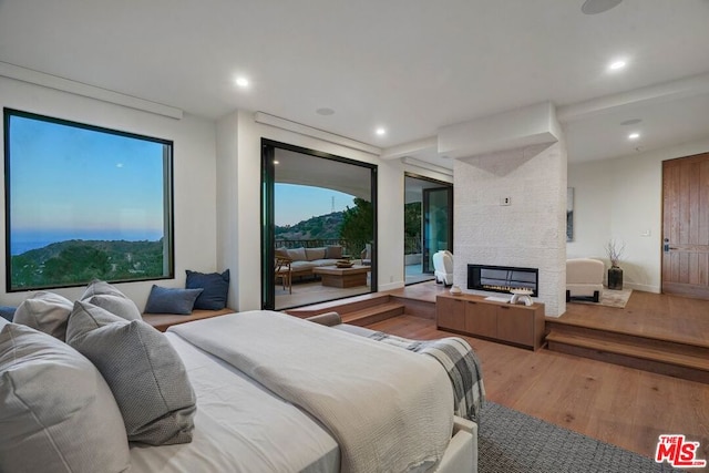 bedroom with a mountain view, hardwood / wood-style floors, access to outside, and a stone fireplace