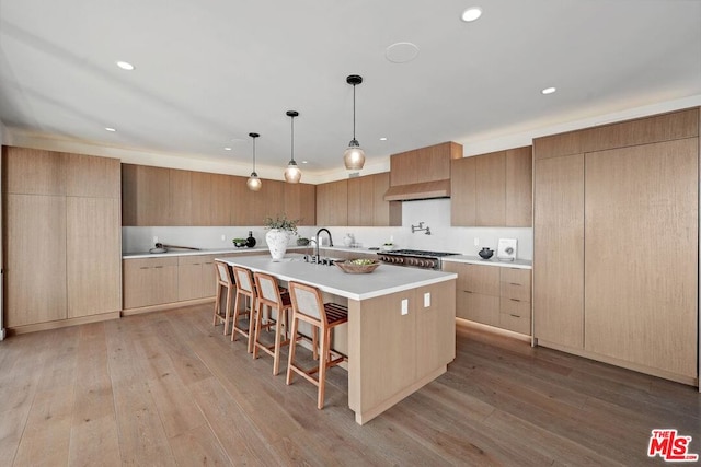 kitchen featuring a kitchen breakfast bar, a center island with sink, pendant lighting, and light hardwood / wood-style flooring