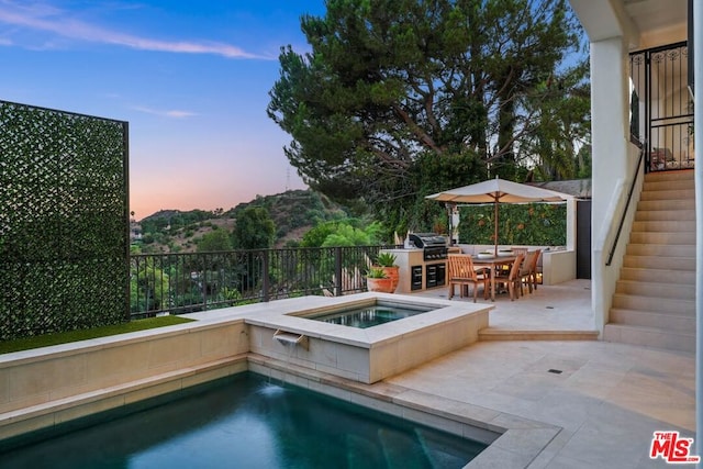 pool at dusk with an in ground hot tub, a patio, and area for grilling