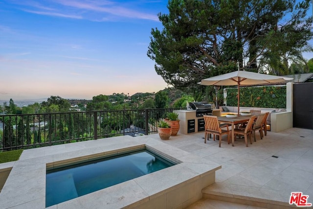 pool at dusk featuring an outdoor kitchen, a patio, and grilling area