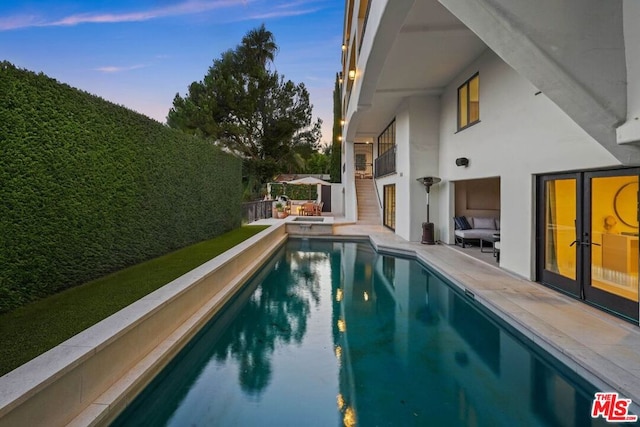 pool at dusk with a patio area and french doors