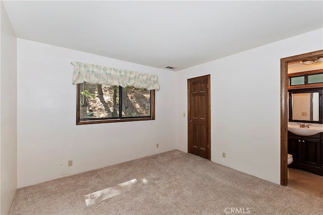 unfurnished bedroom featuring sink, light carpet, and ensuite bath