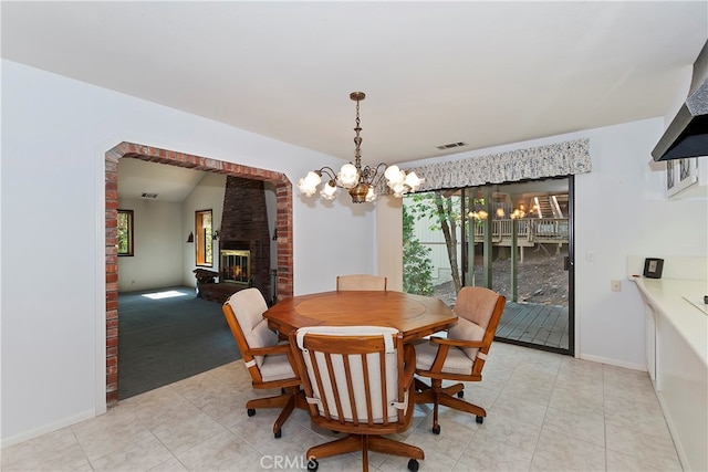 dining area featuring a brick fireplace, light tile patterned floors, and a chandelier