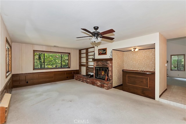 unfurnished living room featuring a brick fireplace, ceiling fan, and light colored carpet