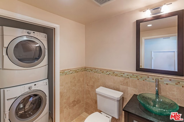 bathroom featuring vanity, tile walls, stacked washer / dryer, and toilet