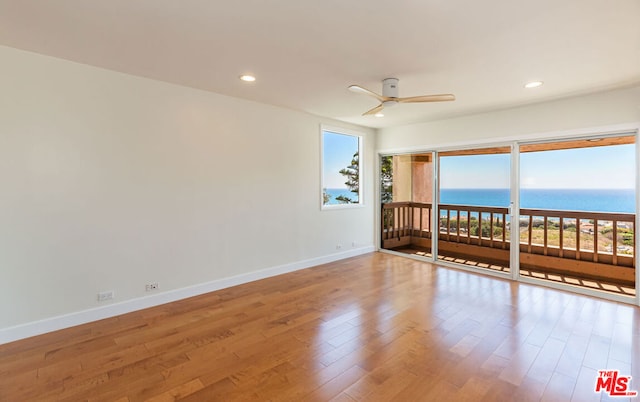 empty room with ceiling fan, hardwood / wood-style floors, and a water view