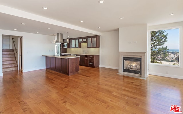 kitchen featuring decorative light fixtures, a center island with sink, light wood-type flooring, and a fireplace