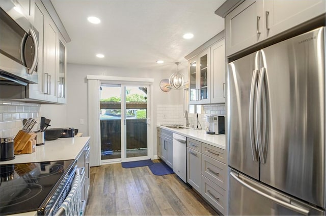 kitchen with appliances with stainless steel finishes, backsplash, sink, wood-type flooring, and hanging light fixtures