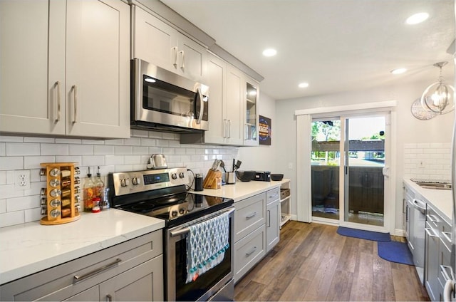 kitchen with gray cabinetry, pendant lighting, appliances with stainless steel finishes, tasteful backsplash, and dark hardwood / wood-style flooring