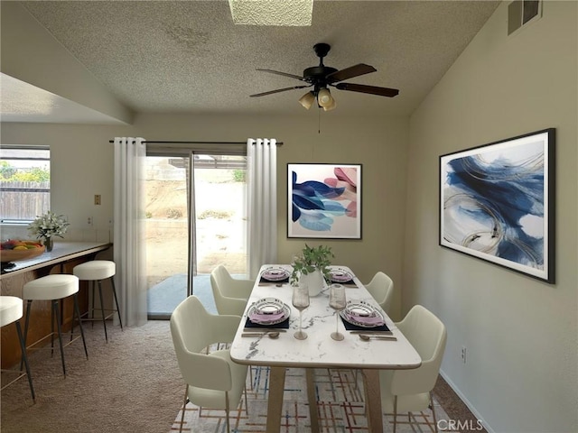 dining space featuring light colored carpet, a healthy amount of sunlight, and a textured ceiling