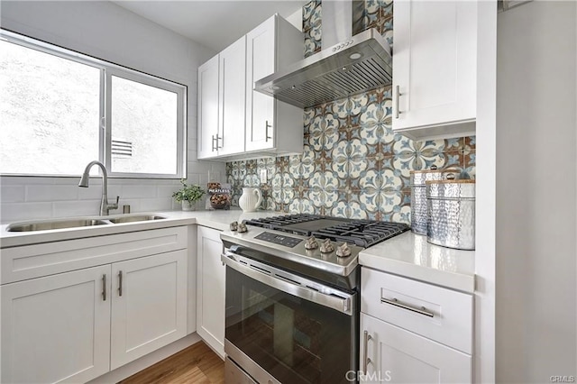 kitchen featuring tasteful backsplash, white cabinets, stainless steel range with gas cooktop, sink, and wall chimney range hood