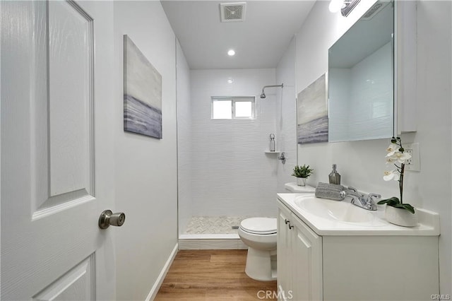 bathroom with a tile shower, vanity, hardwood / wood-style floors, and toilet