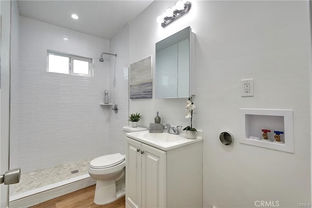 bathroom with a tile shower, hardwood / wood-style floors, vanity, and toilet