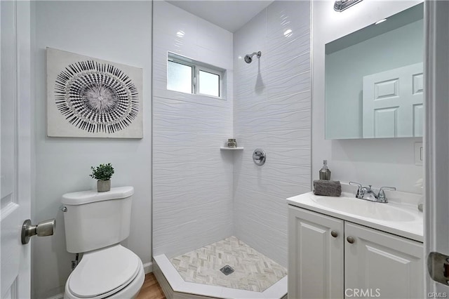 bathroom featuring a tile shower, vanity, and toilet