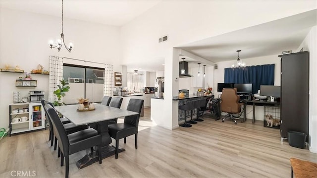 dining space featuring a notable chandelier, visible vents, light wood-type flooring, and a high ceiling