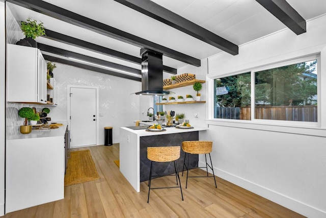 bar with light wood-type flooring, a wealth of natural light, island range hood, and white cabinets