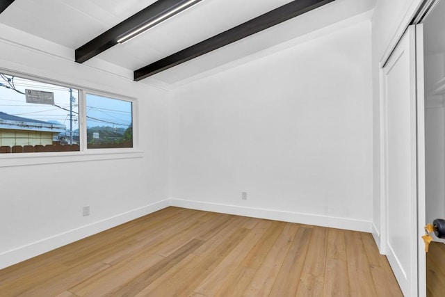 empty room featuring light hardwood / wood-style floors and vaulted ceiling with beams