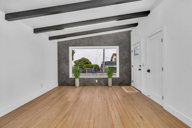 unfurnished living room with tile walls, beam ceiling, and light wood-type flooring