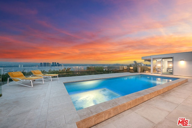 pool at dusk featuring a patio and an in ground hot tub