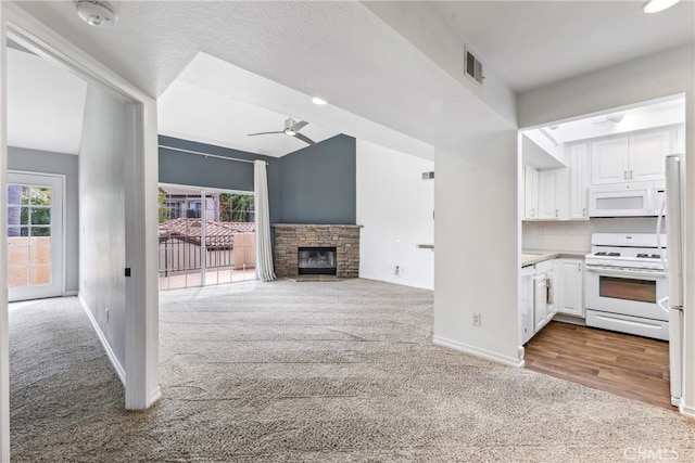 unfurnished living room featuring light carpet, a stone fireplace, a textured ceiling, and ceiling fan