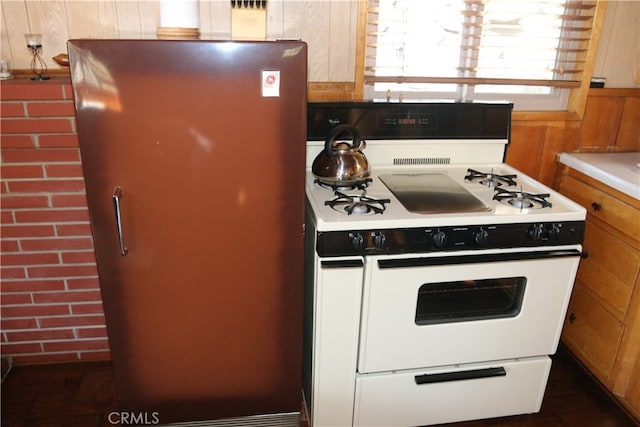 kitchen featuring wooden walls, white range oven, and refrigerator