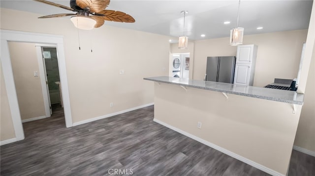 kitchen with kitchen peninsula, decorative light fixtures, stacked washing maching and dryer, stainless steel refrigerator, and a breakfast bar area