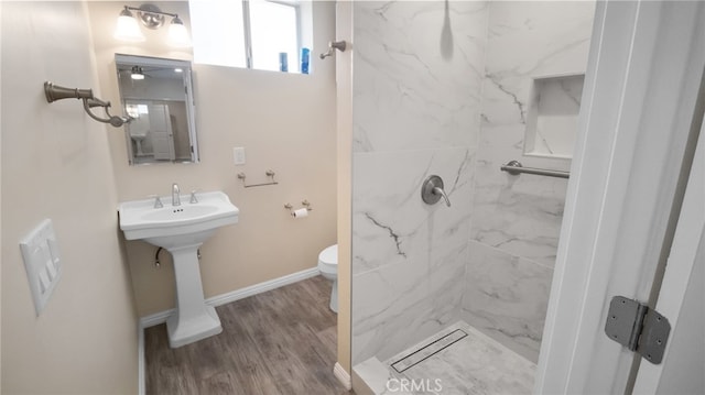 bathroom featuring toilet, hardwood / wood-style floors, a tile shower, and sink