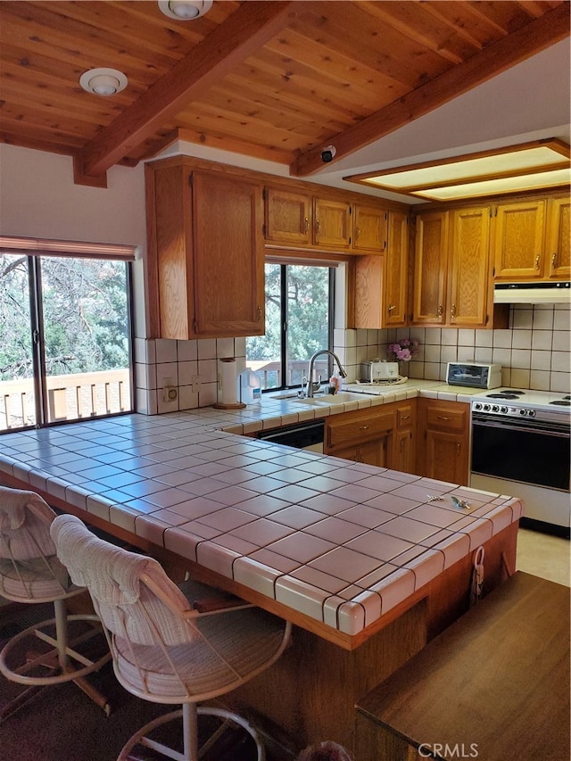 kitchen featuring electric stove, tile counters, kitchen peninsula, and a breakfast bar