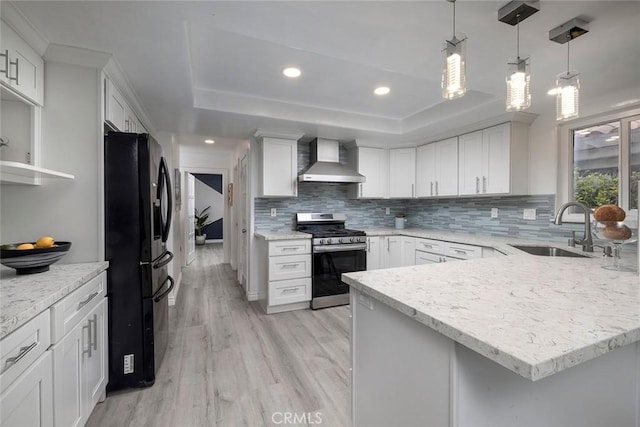 kitchen featuring white cabinets, black fridge, sink, stainless steel stove, and wall chimney exhaust hood