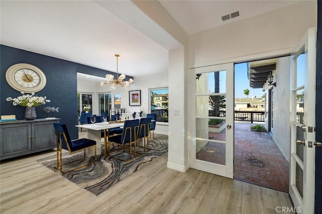 dining space with french doors, light hardwood / wood-style floors, and a notable chandelier