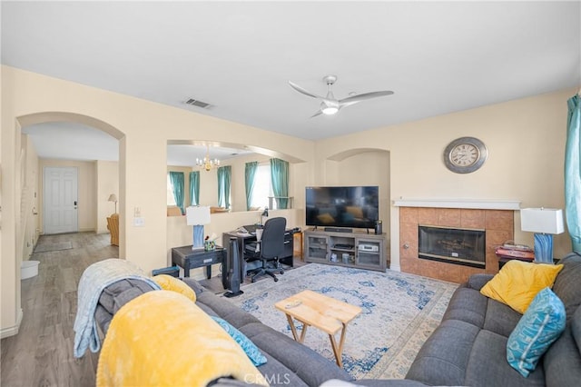 living area featuring arched walkways, a fireplace, visible vents, wood finished floors, and ceiling fan with notable chandelier