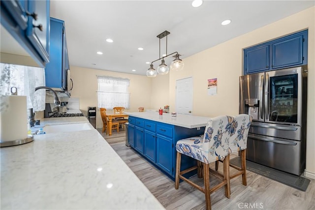 kitchen with a center island, stainless steel appliances, a sink, blue cabinets, and light wood-type flooring