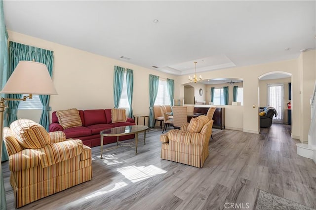 living area with arched walkways, a raised ceiling, a notable chandelier, and wood finished floors