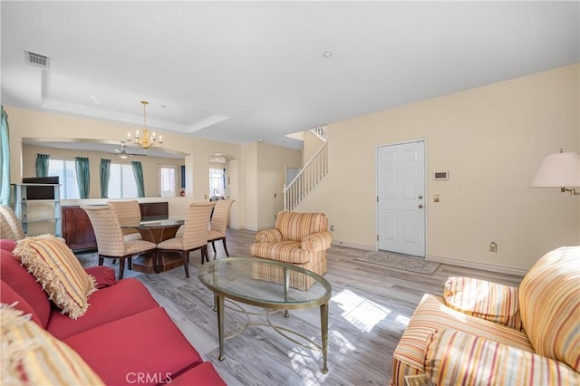 living area featuring a notable chandelier, a raised ceiling, visible vents, light wood-type flooring, and stairs